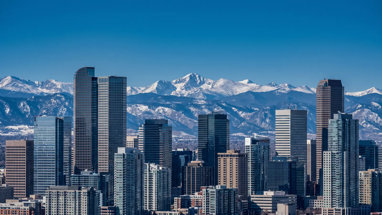 The Denver skyline with the snow covered Front Range rising behind it under a clear high-altitude sky