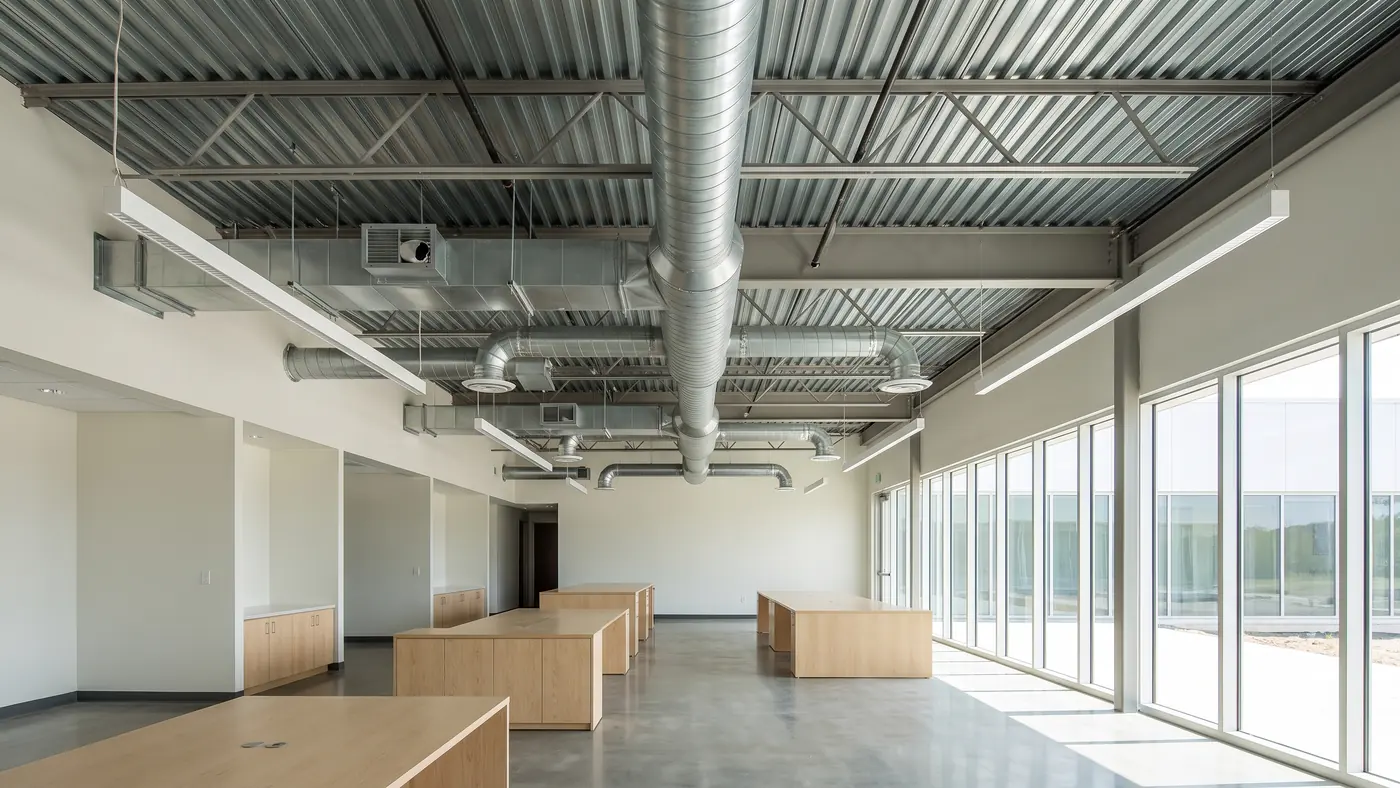 A modern open plan office with an exposed structural ceiling, spiral round ductwork, a rectangular trunk duct and VAV terminal boxes overhead
